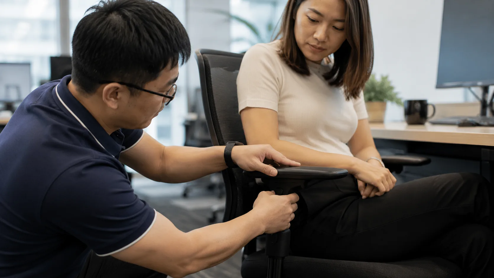 An ergonomics specialist adjusting the armrest height on an employee's office chair in Singapore