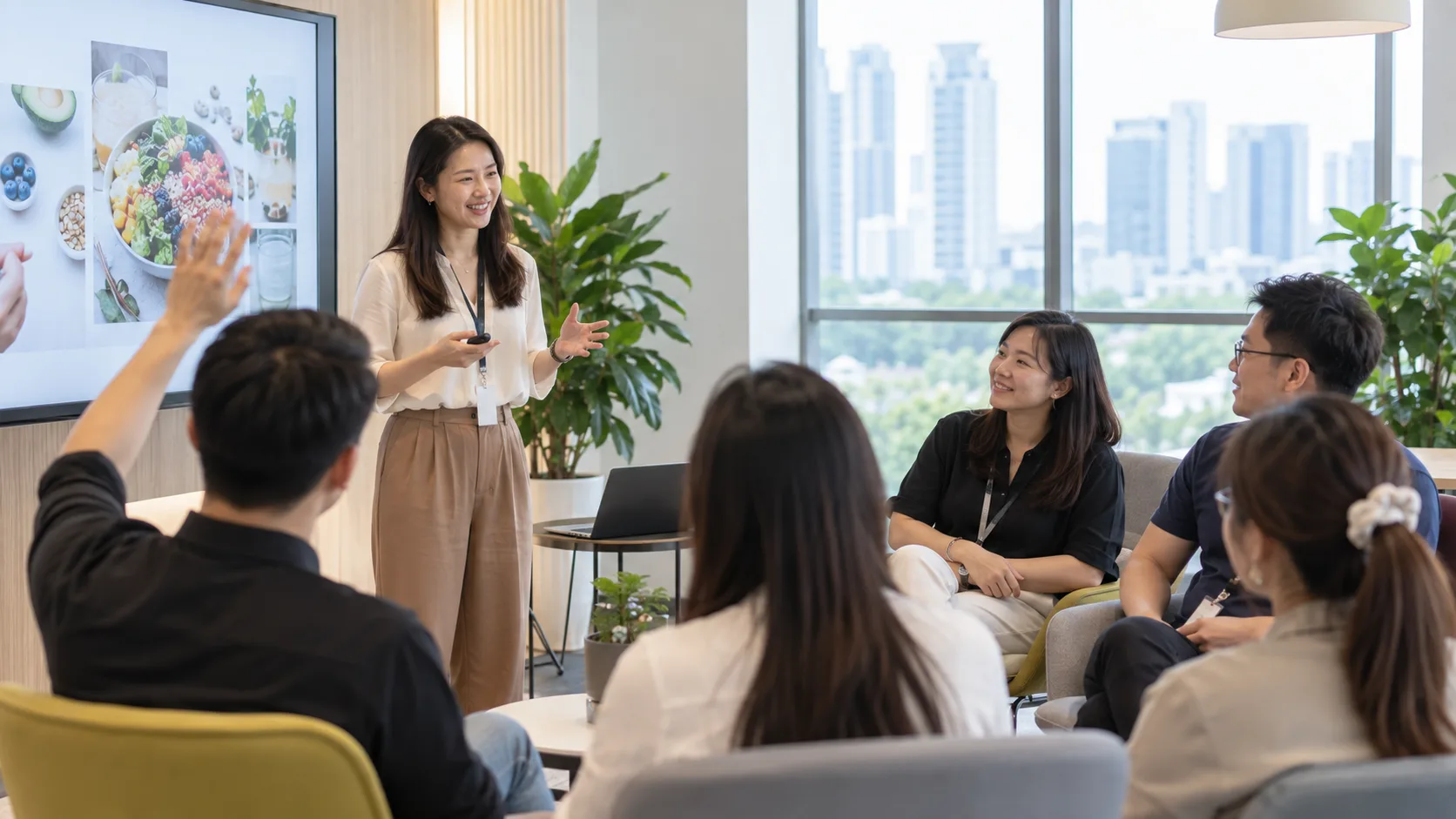 A facilitator running a nutrition and wellness workshop in a Singapore office, employees seated in a relaxed semi-circle with one raising a hand to ask a question