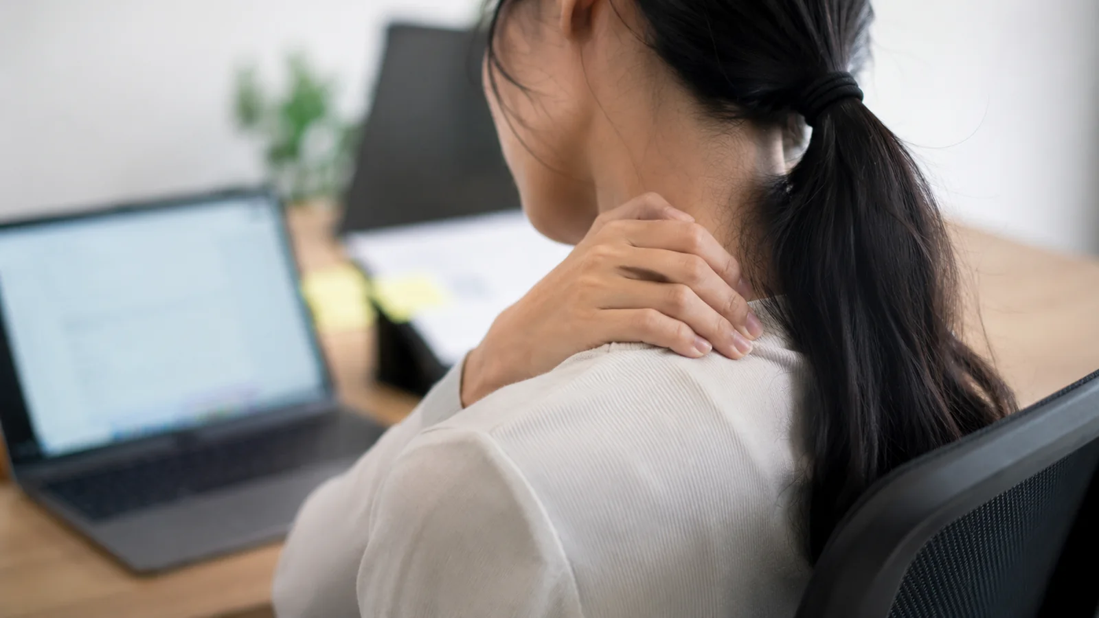 An office worker experiencing neck and shoulder pain at her desk