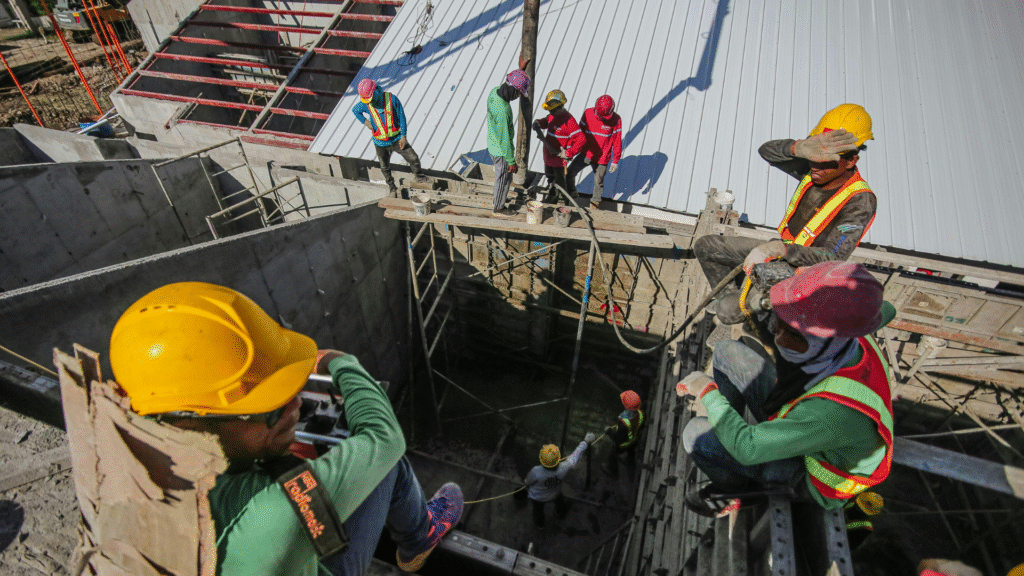 Group of construction workers wearing helmets and vests working on scaffolding at a construction site in Singapore.