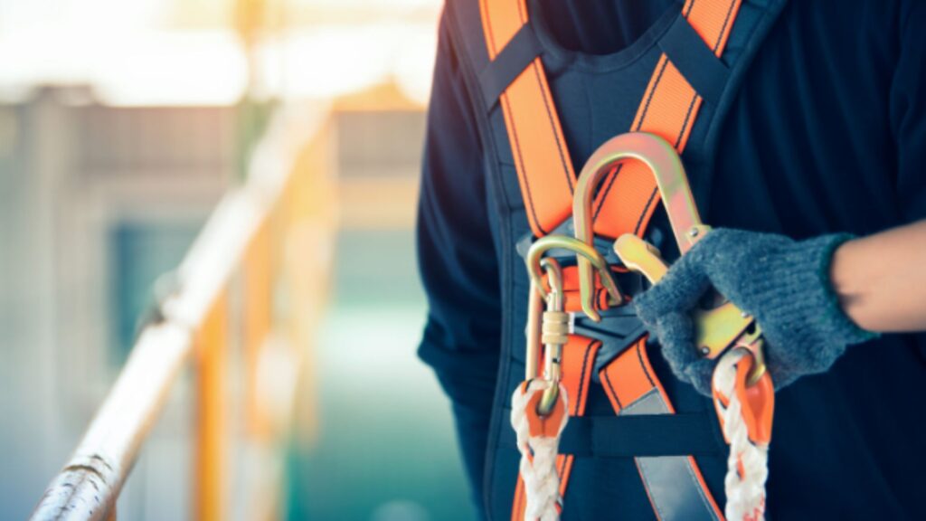 Worker checking safety harness and carabiner before working at height, promoting workplace safety awareness