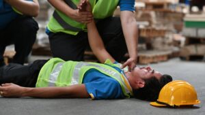 Worker lying on factory floor while coworker checks for injuries