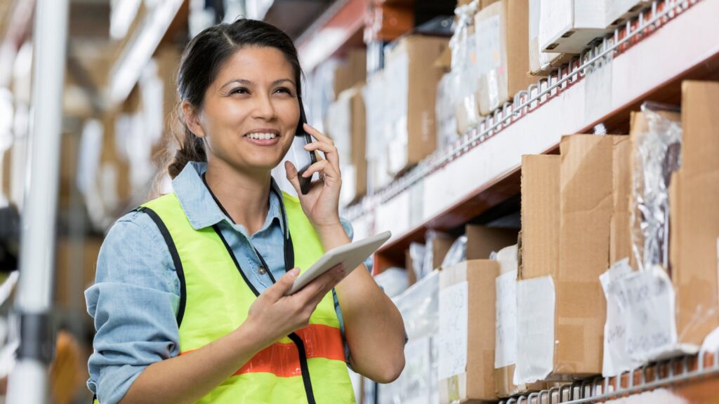 Warehouse worker on phone and holding a tablet while working