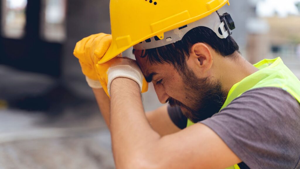 Construction worker holding helmet and looking fatigued at job site