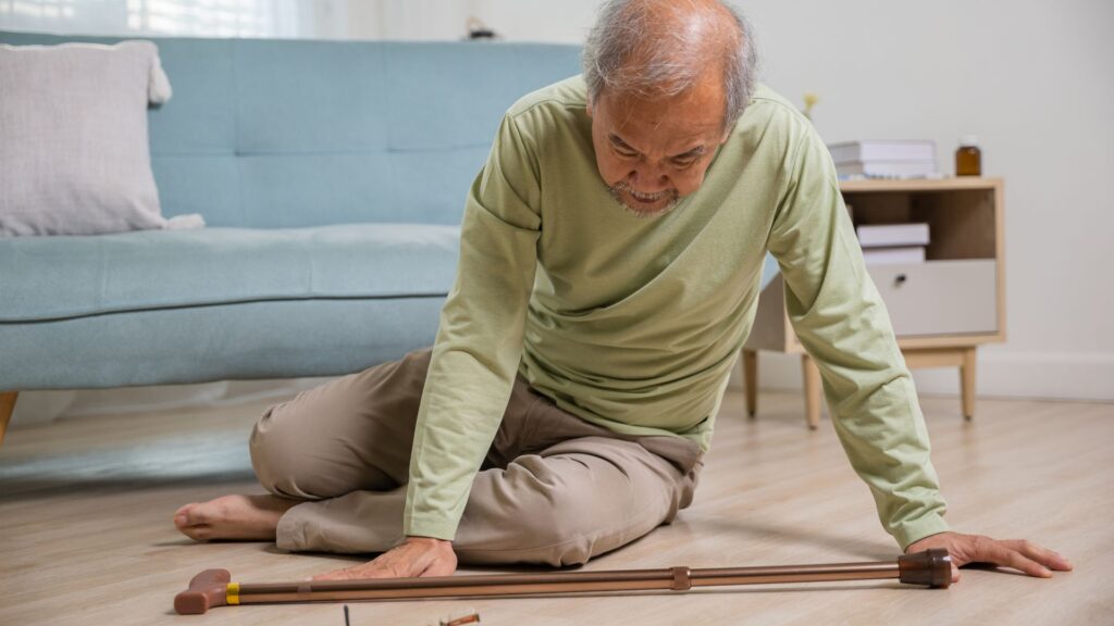 Elderly man sitting on floor reaching for walking cane after losing balance