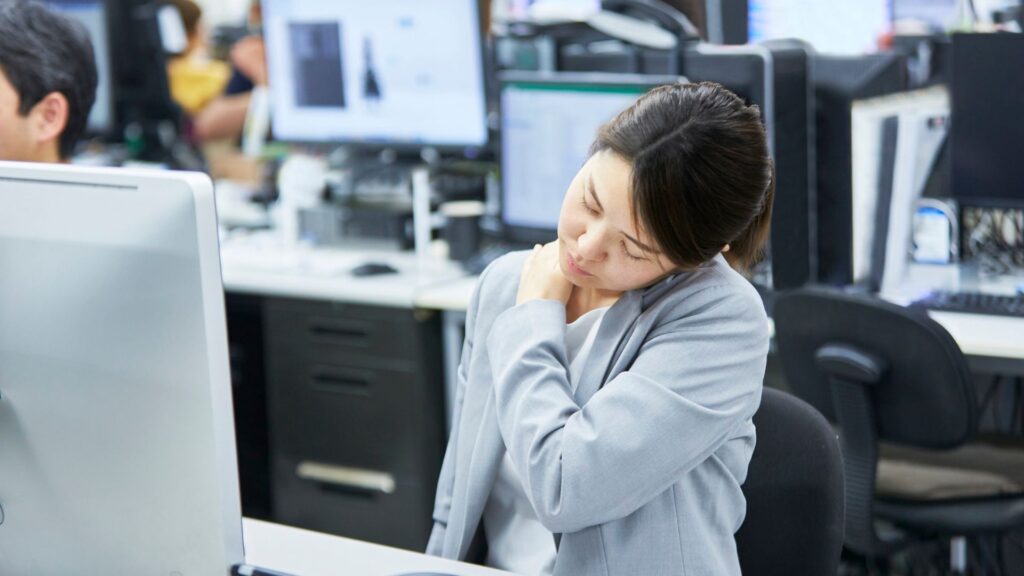 Office employee experiencing neck and shoulder discomfort due to poor workstation ergonomics in Singapore