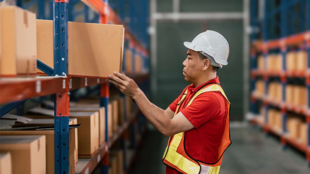 Worker lifting and reaching for boxes in a warehouse, illustrating common ergonomic risks in the workplace