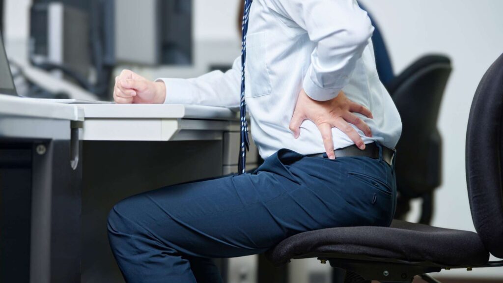 Office worker experiencing lower back discomfort due to prolonged sitting and poor workstation ergonomics