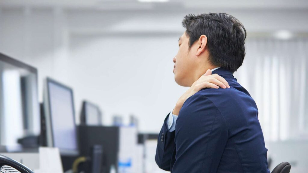 Office employee experiencing shoulder discomfort while working at a desk, highlighting the need for ergonomic risk assessment