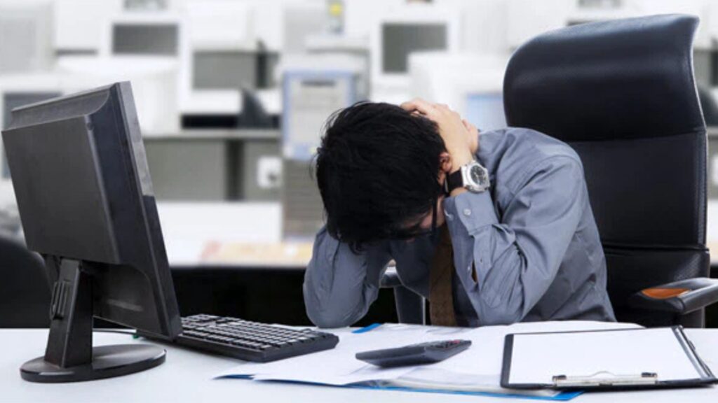 Office worker holding his neck while seated at a computer, illustrating work-related neck strain in an office environment