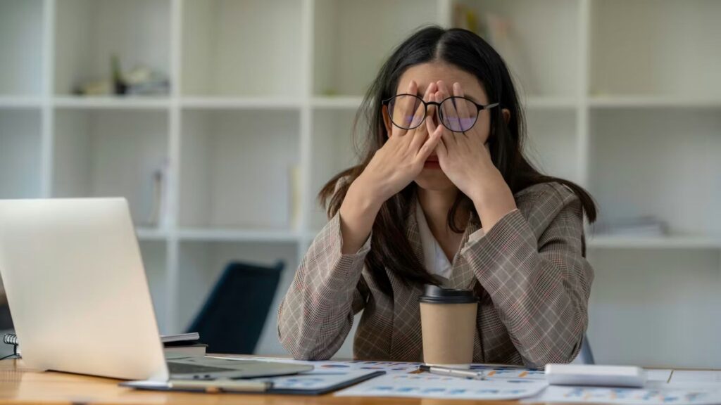 Office worker rubbing her eyes while seated at a desk, illustrating mental fatigue and reduced productivity during work