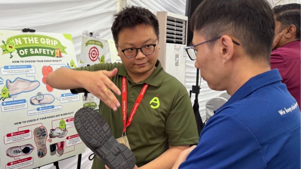 Workplace health educator demonstrating shoe sole wear to an employee using a safety awareness poster
