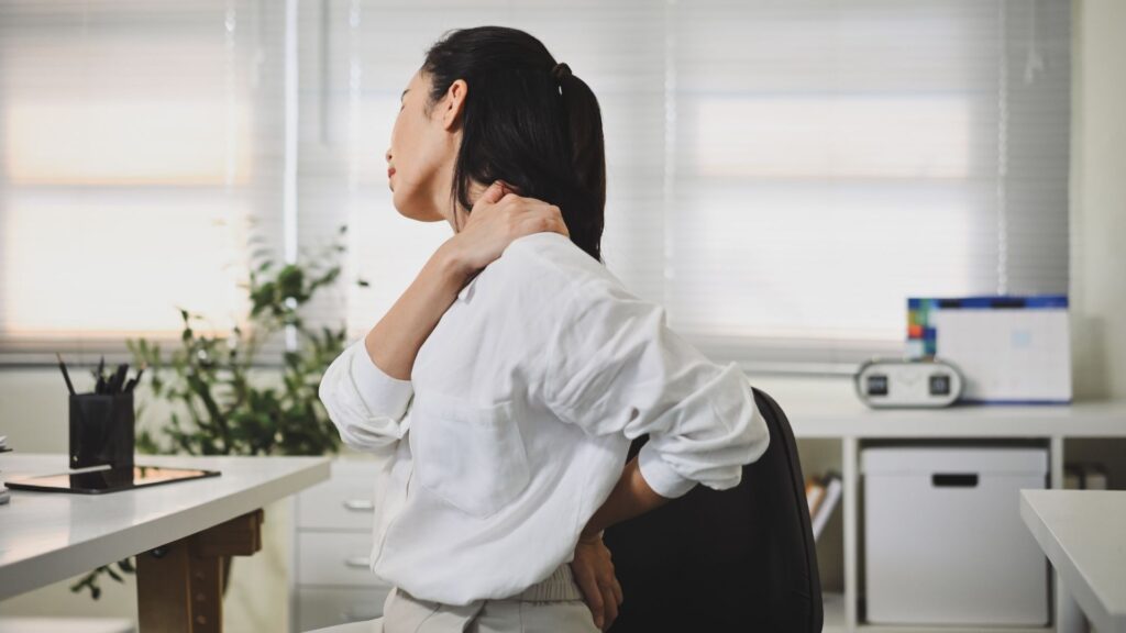 Office worker experiencing neck pain at desk, an early sign of WMSD caused by poor workplace ergonomics