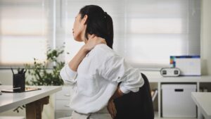 Office worker experiencing neck pain at desk, an early sign of WMSD caused by poor workplace ergonomics